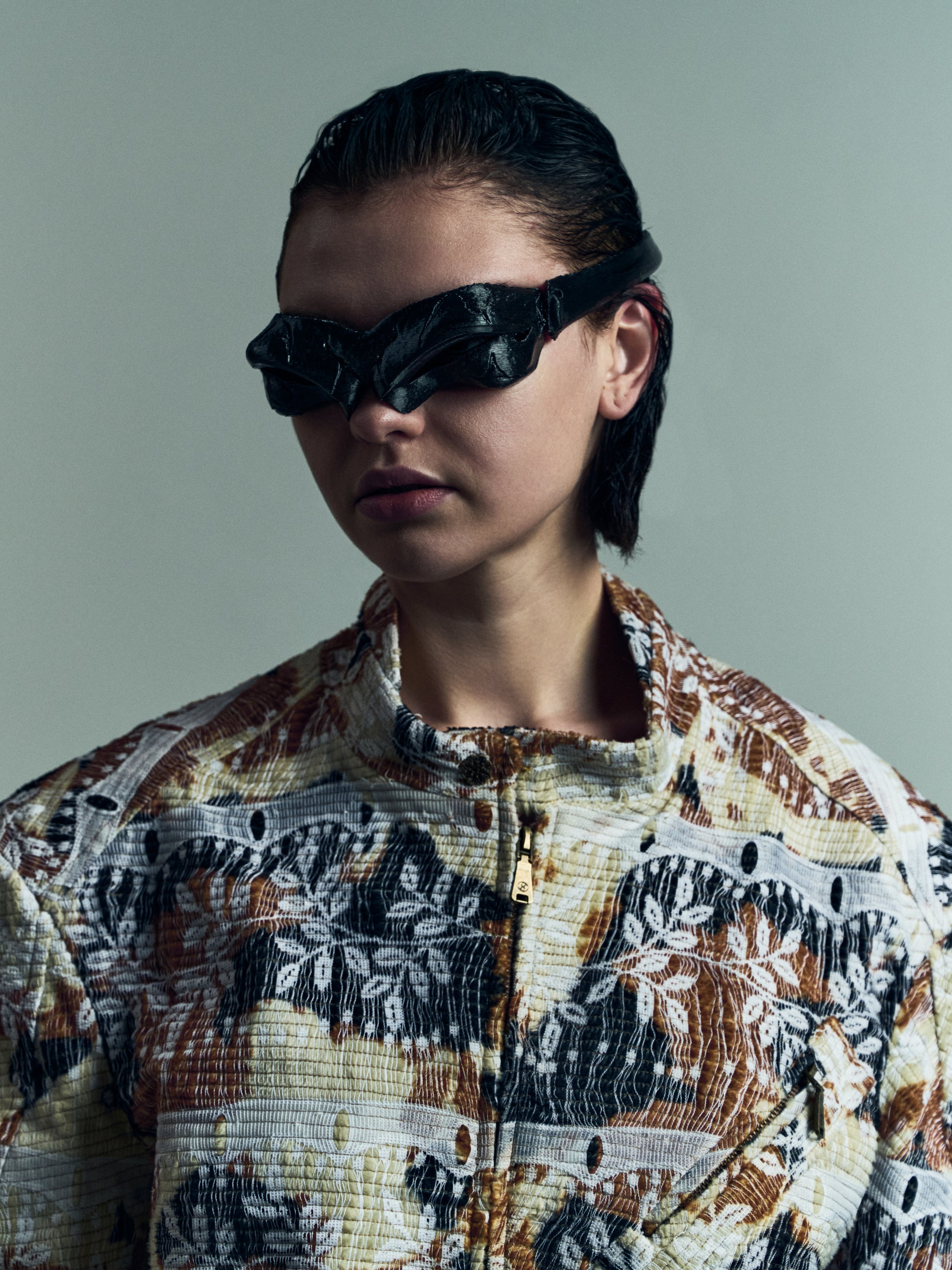 Person wearing a patterned shirt and black sunglasses against a plain background